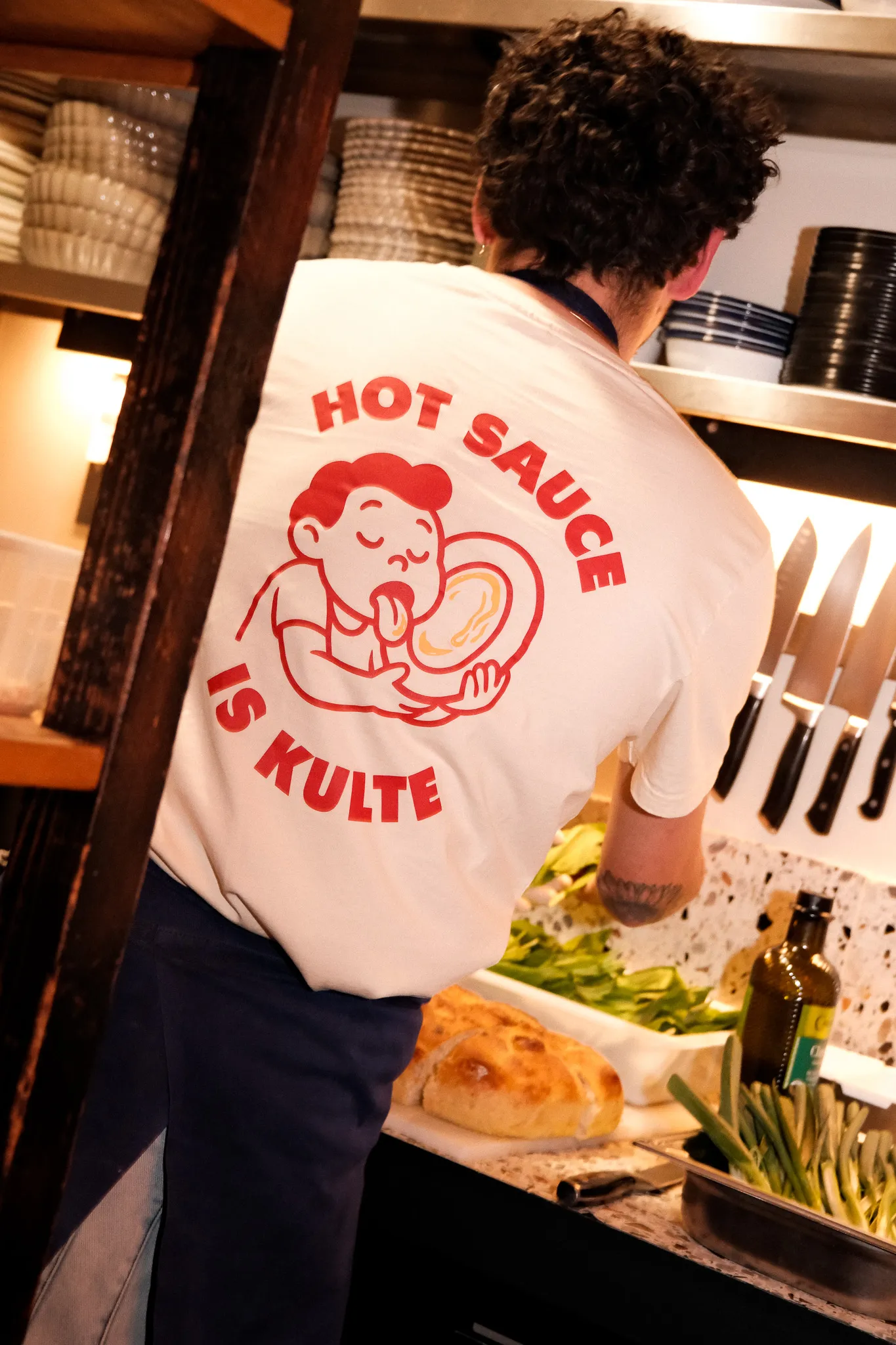 Dos du T-shirt Hot Sauce X Kulte, impression rouge grand format, porté en cuisine